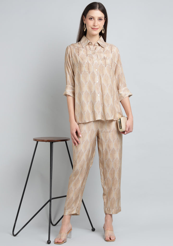 Woman wearing a beige patterned outfit standing next to a black stool on a light gray background